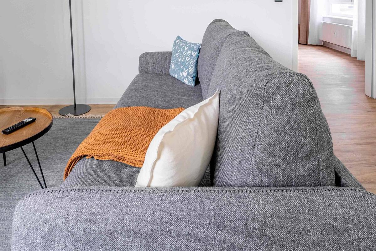 A modern living room with a grey sofa, a floor lamp, and two framed artworks on the wall.