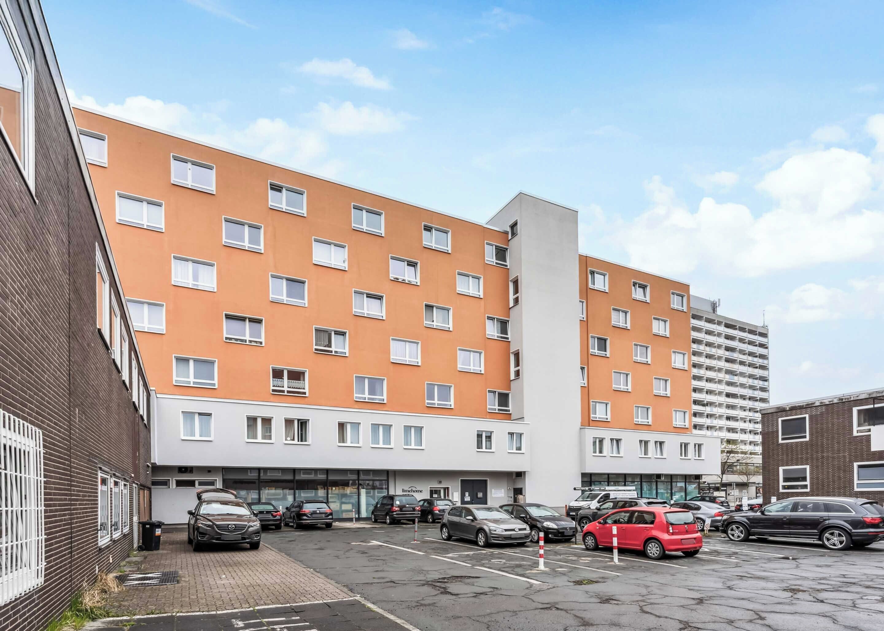A multi-story hotel with a brick facade and orange and white exterior. There are several cars parked in front, and the building has multiple windows per floor.