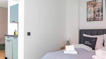 A modern bedroom with a bed, a bedside table, a nightstand, a hanging light fixture, a wall-mounted picture, and a mirror.