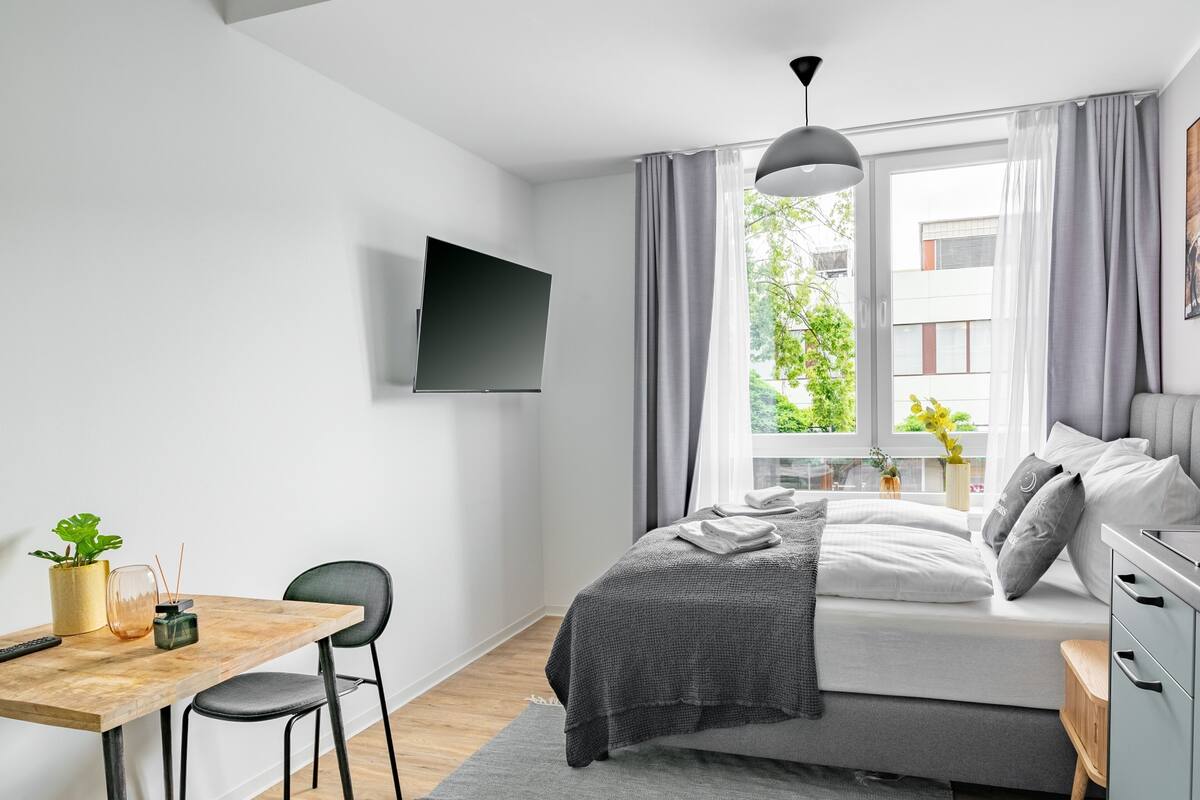 A modern bedroom with a bed, bedside table, TV, and a window with curtains.