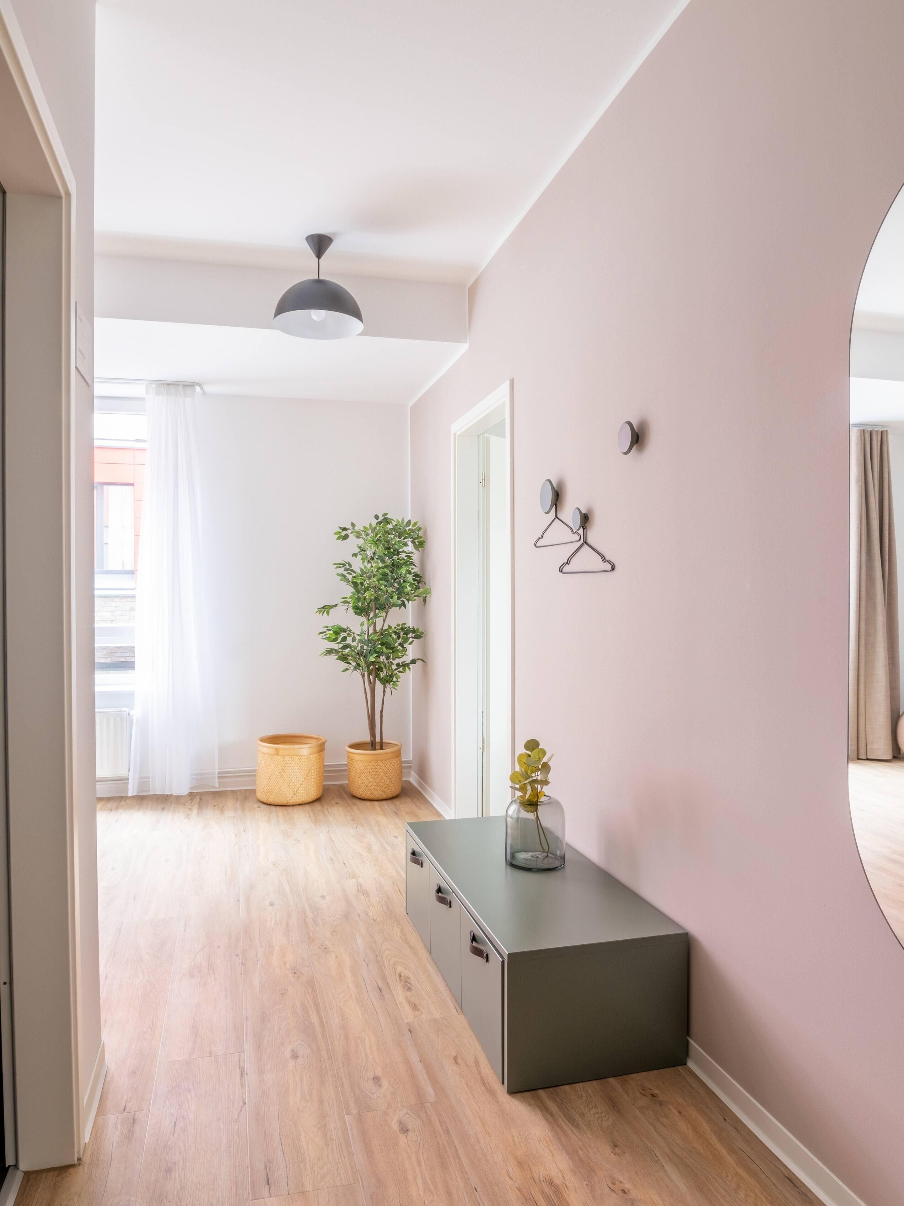 A hallway with wooden flooring, a grey cabinet, a potted plant, and a mirror on the wall.