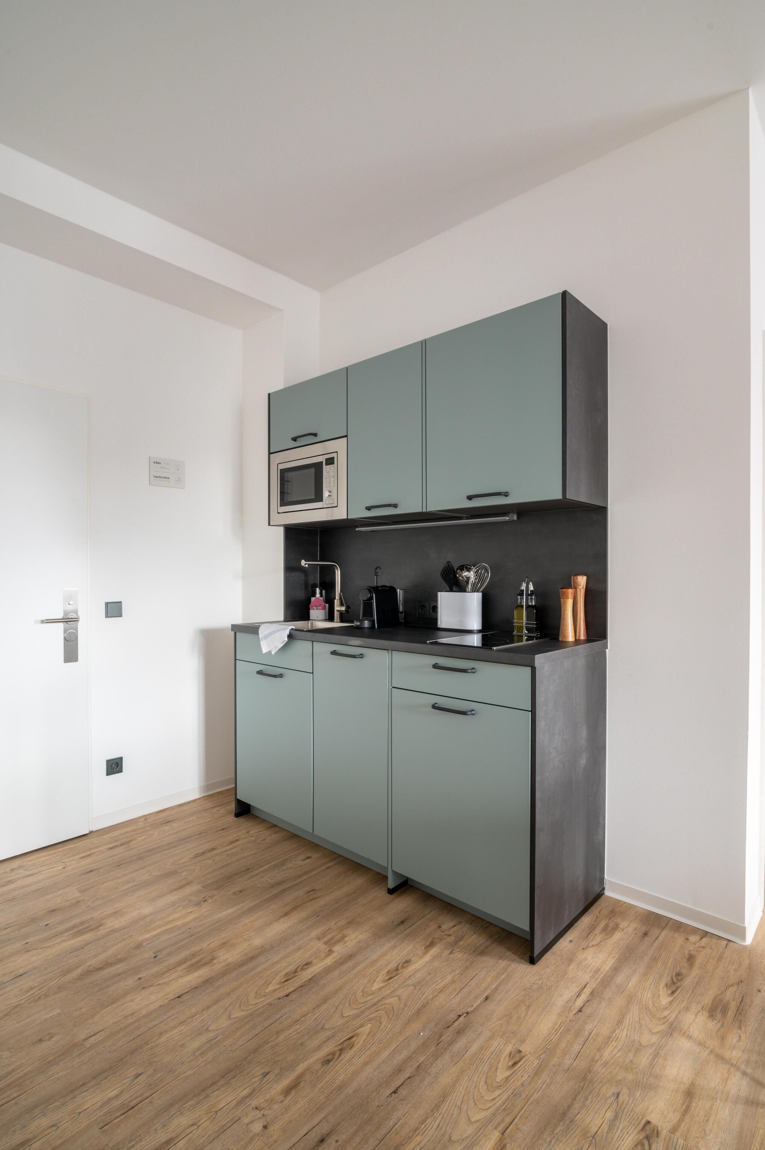 Een moderne keuken met smaragdgroene kastjes, een magnetron en een spoelbak.