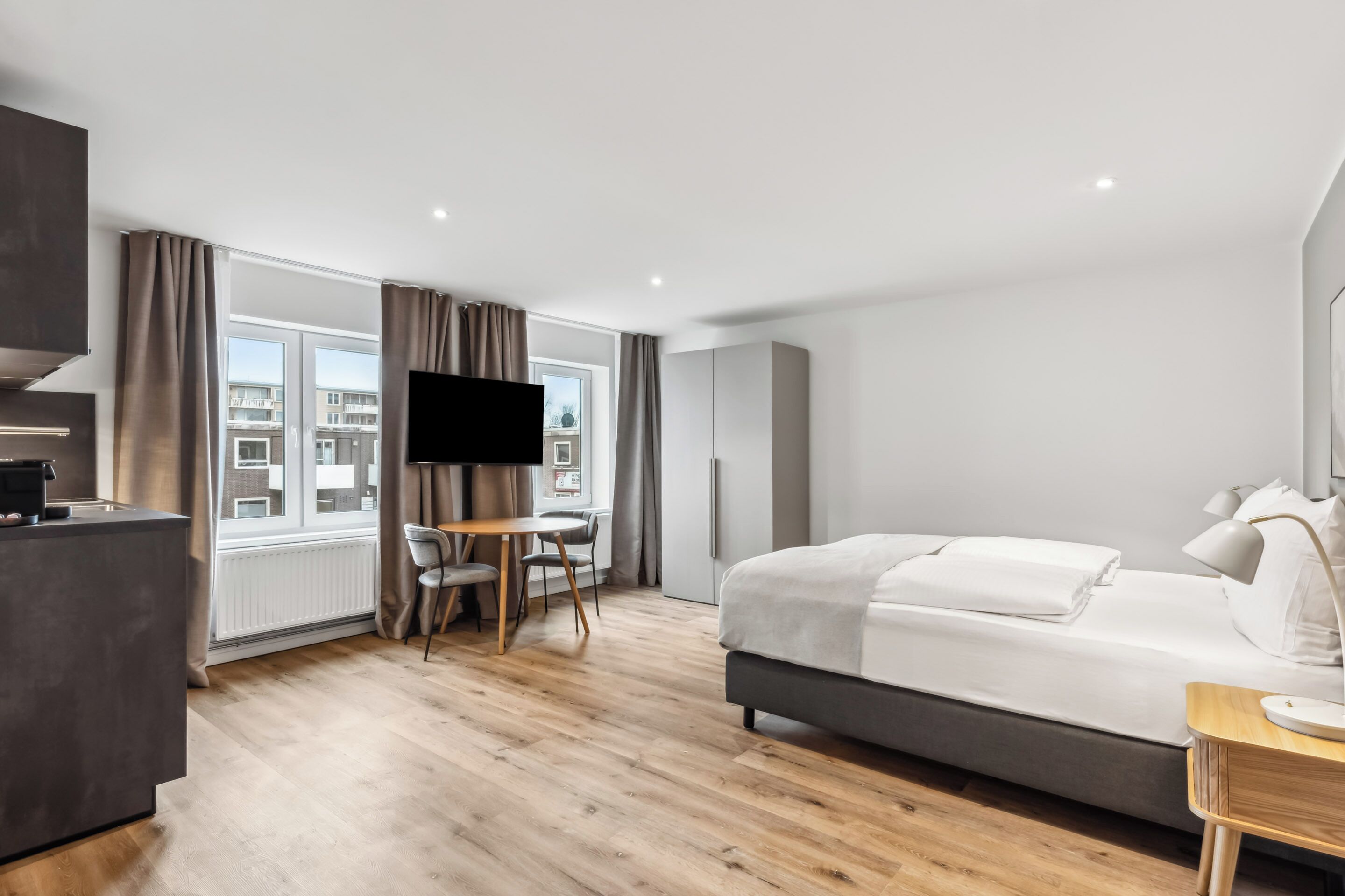 Une chambre d’hôtel moderne dotée d’un grand lit, d’un bureau avec une chaise, d’une télévision et offrant une vue sur la ville grâce à de grandes fenêtres.