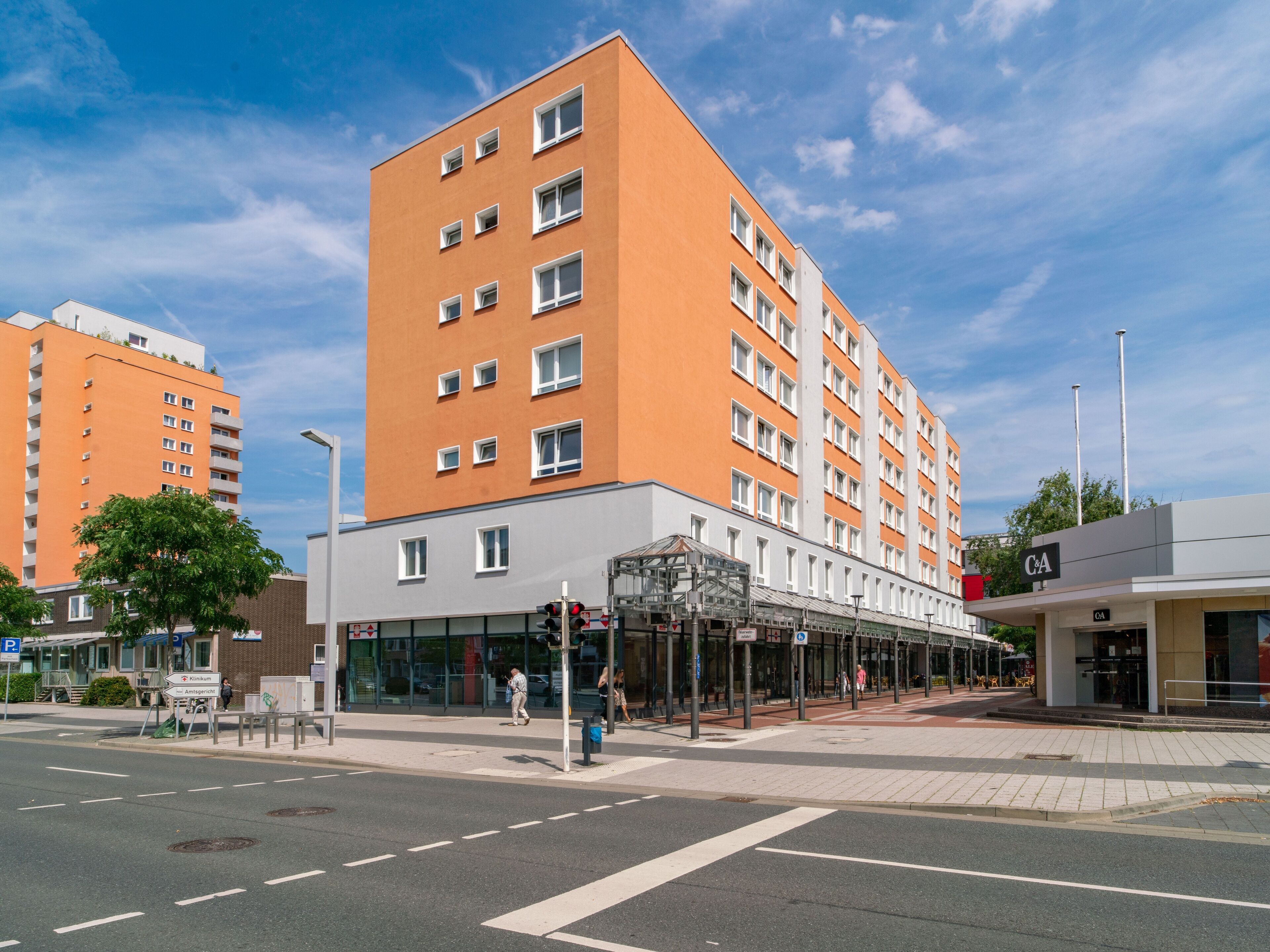 Un hotel moderno con diversi piani, una zona commerciale a livello strada e un cielo sereno.