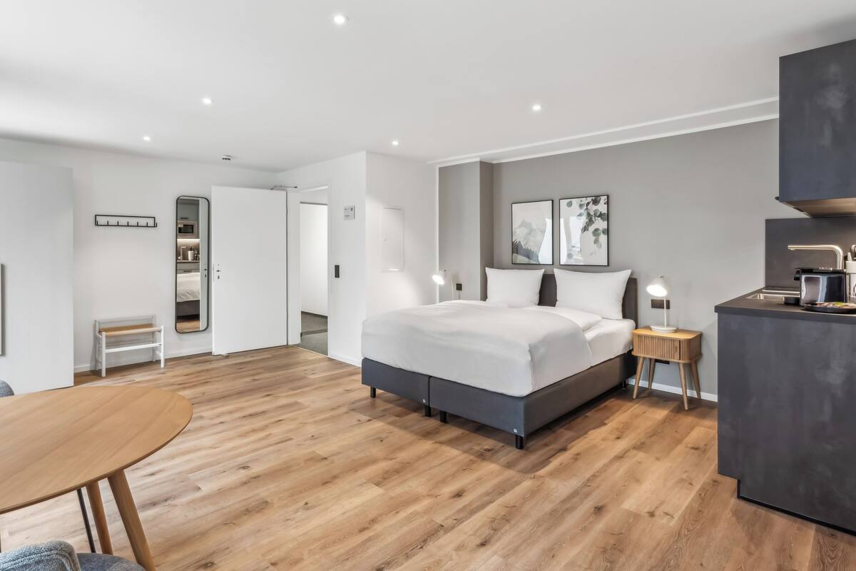 A modern hotel room with a large bed, bedside tables, a desk, and a wardrobe.