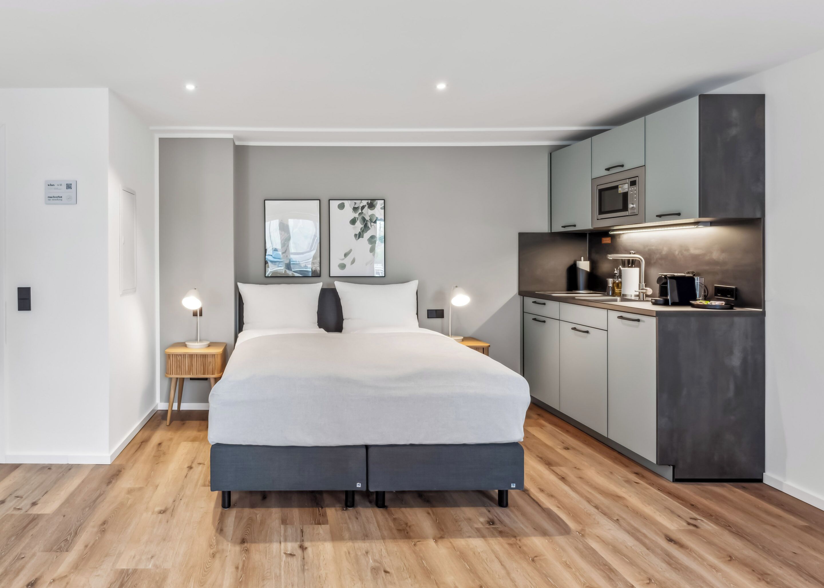 A modern bedroom with a large bed, bedside tables, a built-in kitchen with a microwave, and a small countertop.