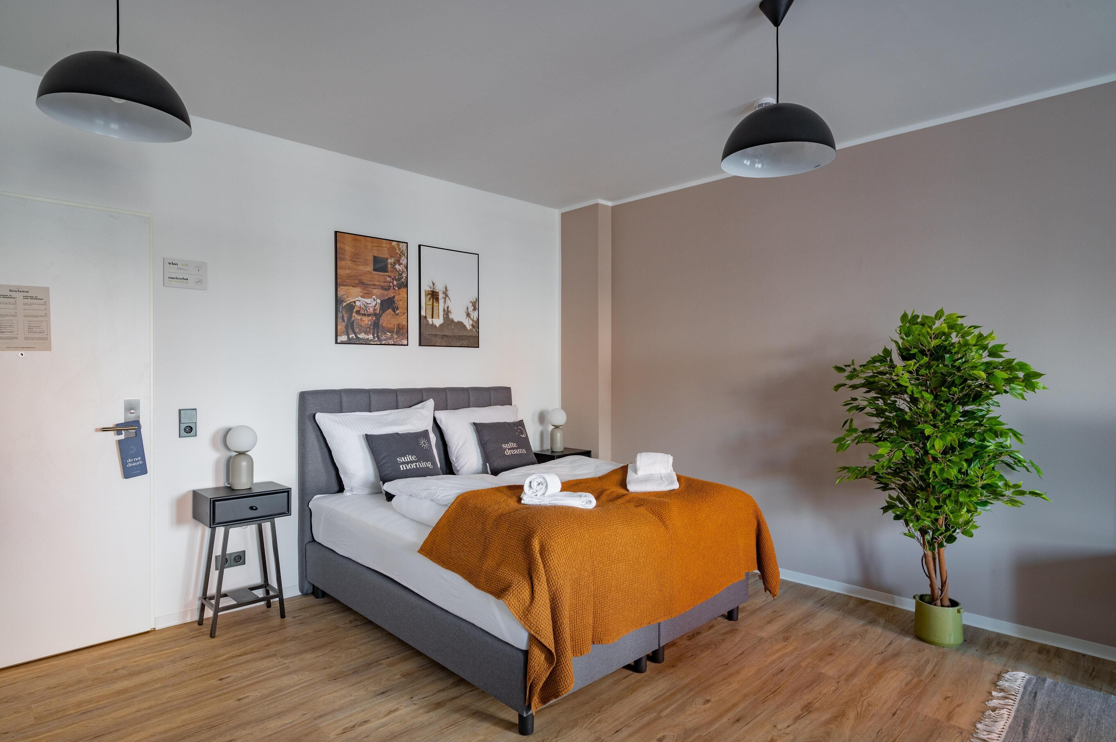 Et moderne hotelværelse med seng, sengeborde, en stueplante og kunst på væggen.