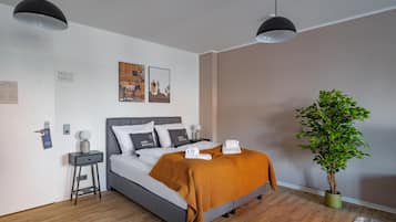 Et moderne hotelværelse med seng, sengeborde, en stueplante og kunst på væggen.