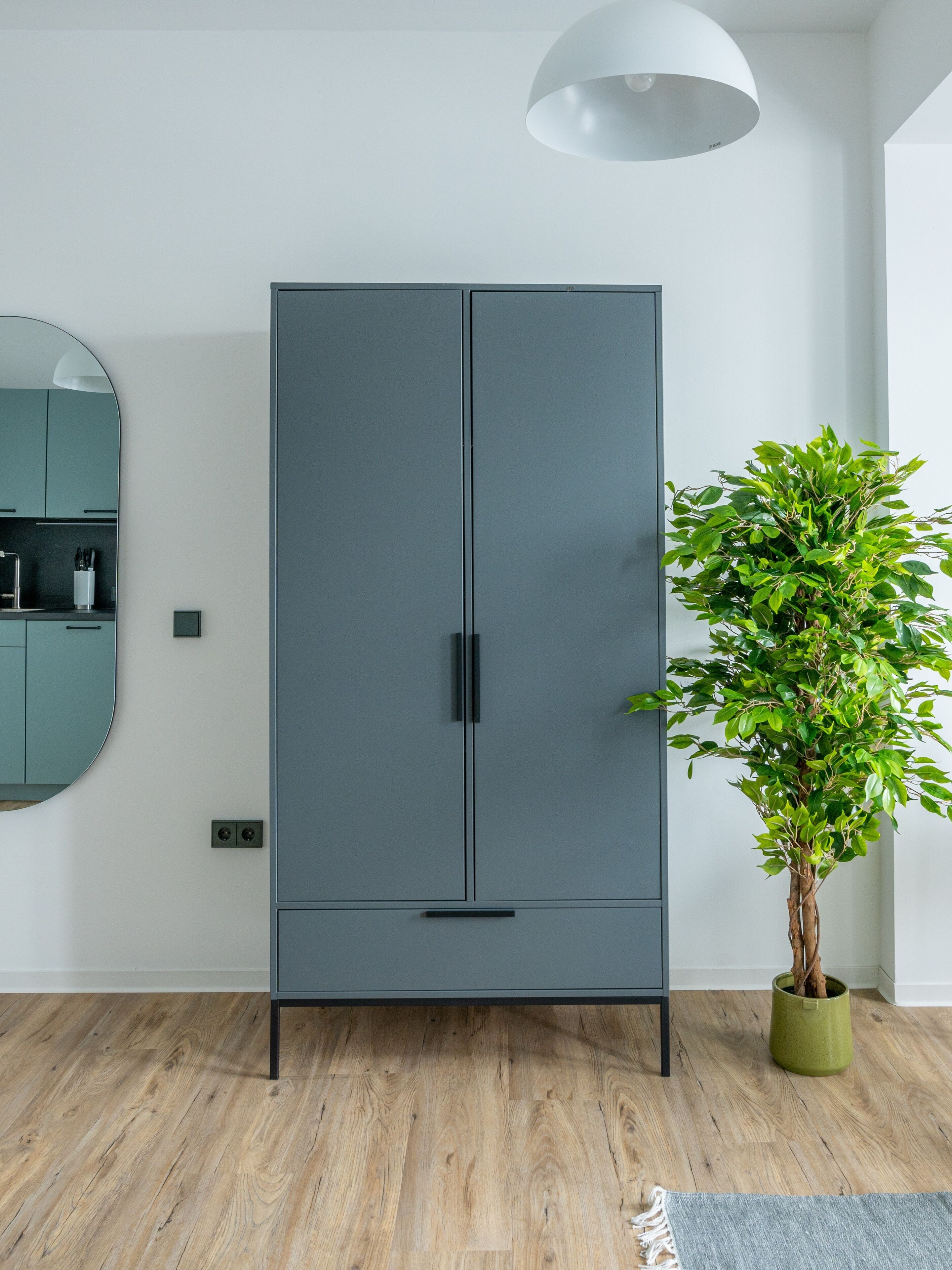Ein modernes Zimmer mit einem grauen Kleiderschrank, einem runden Spiegel und einem Blumentopf.