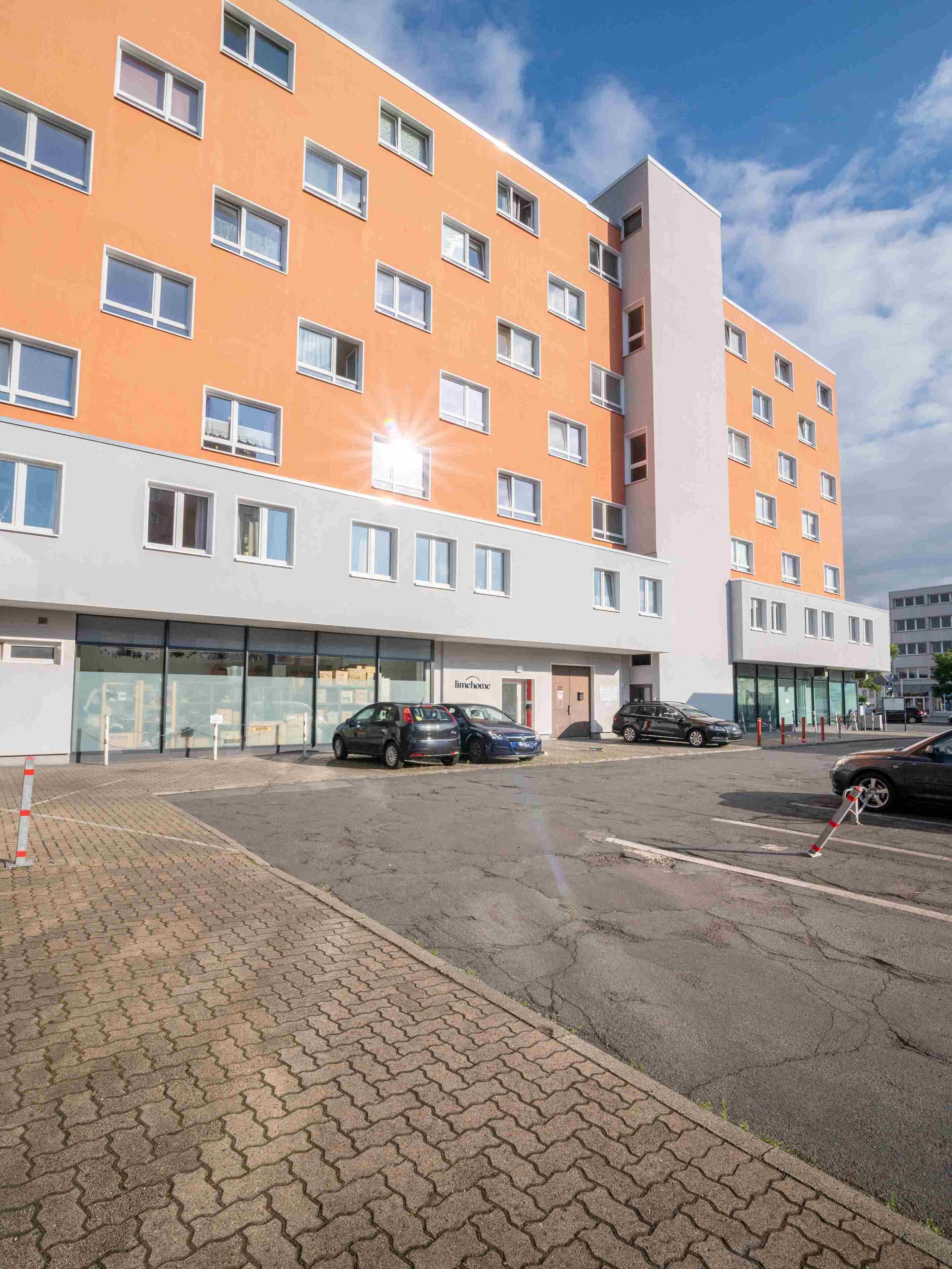 A multi-story hotel with orange and white exterior walls, a parking lot, and several cars parked in front.