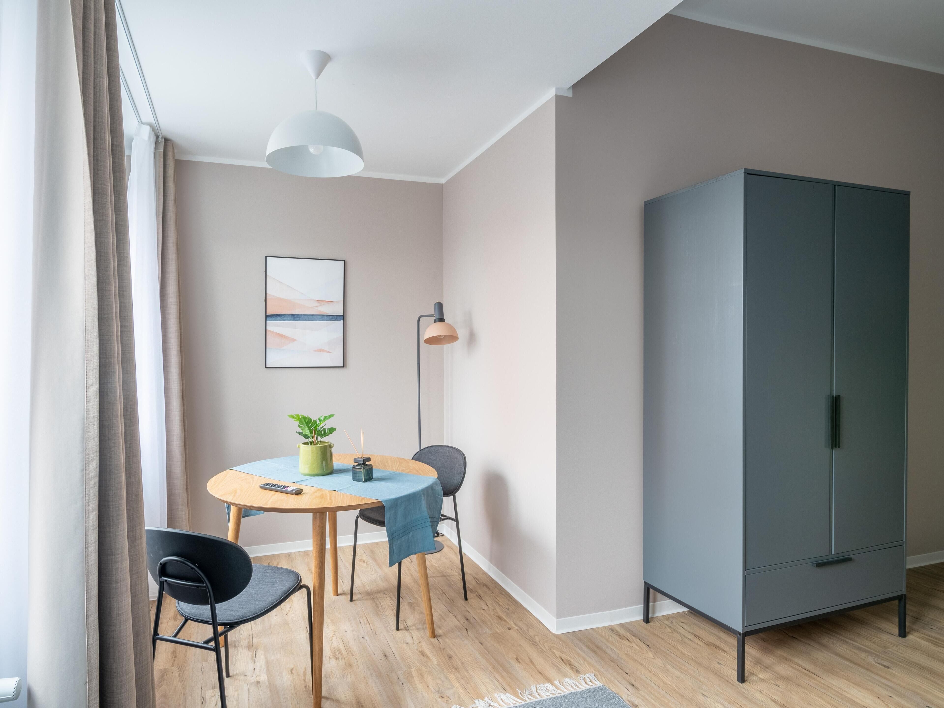 A modern room with a dining table, chairs, a cabinet, and a hanging light fixture.