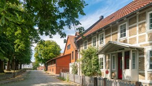 A cobblestone street lined with traditional brick houses, a white picket fence, and mature trees. - Limehome Salzgitter A.-Schweitzer-Str. (Salzgitter)