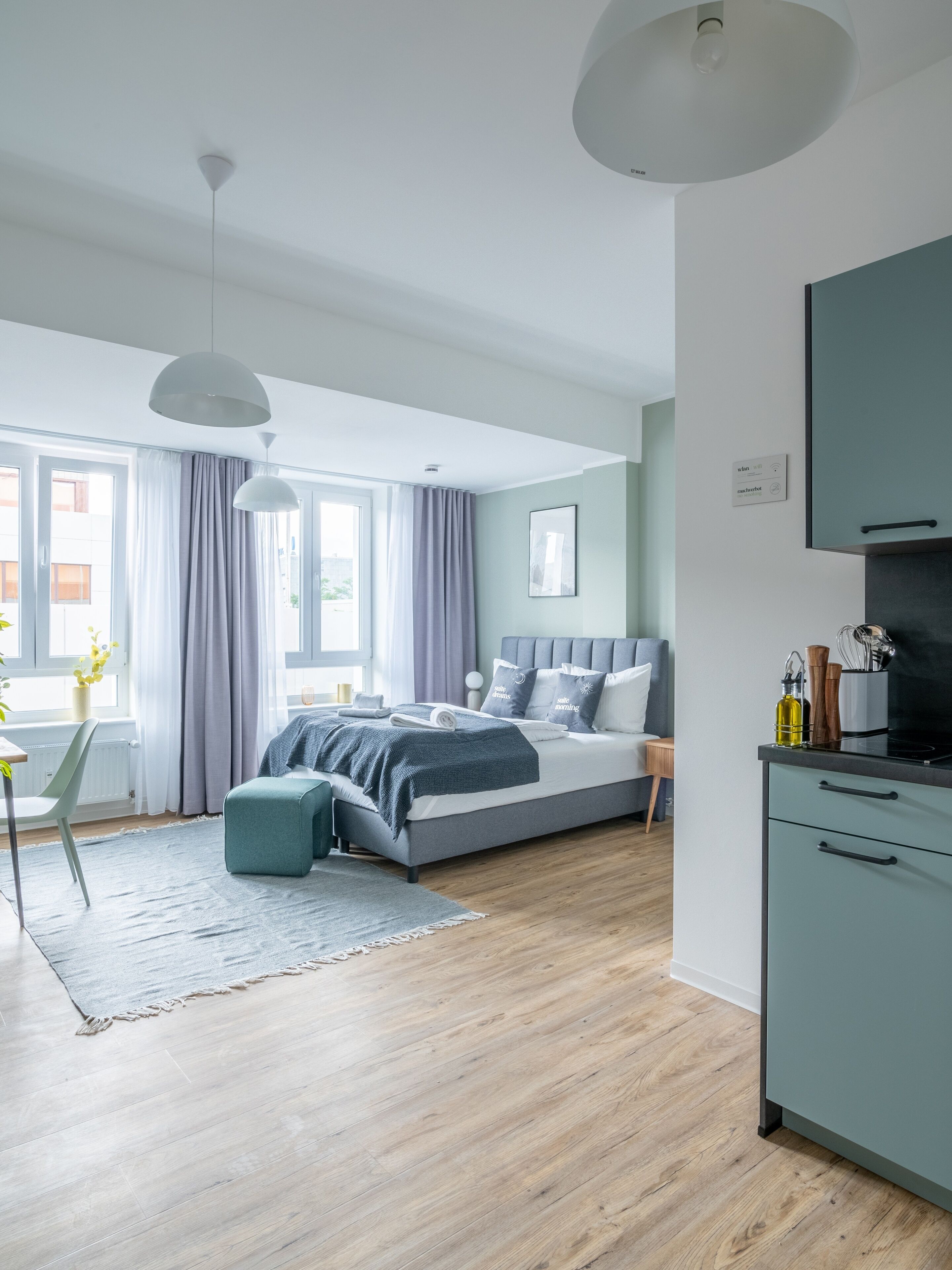 A modern bedroom with a bed, bedside tables, a desk, and a kitchenette.