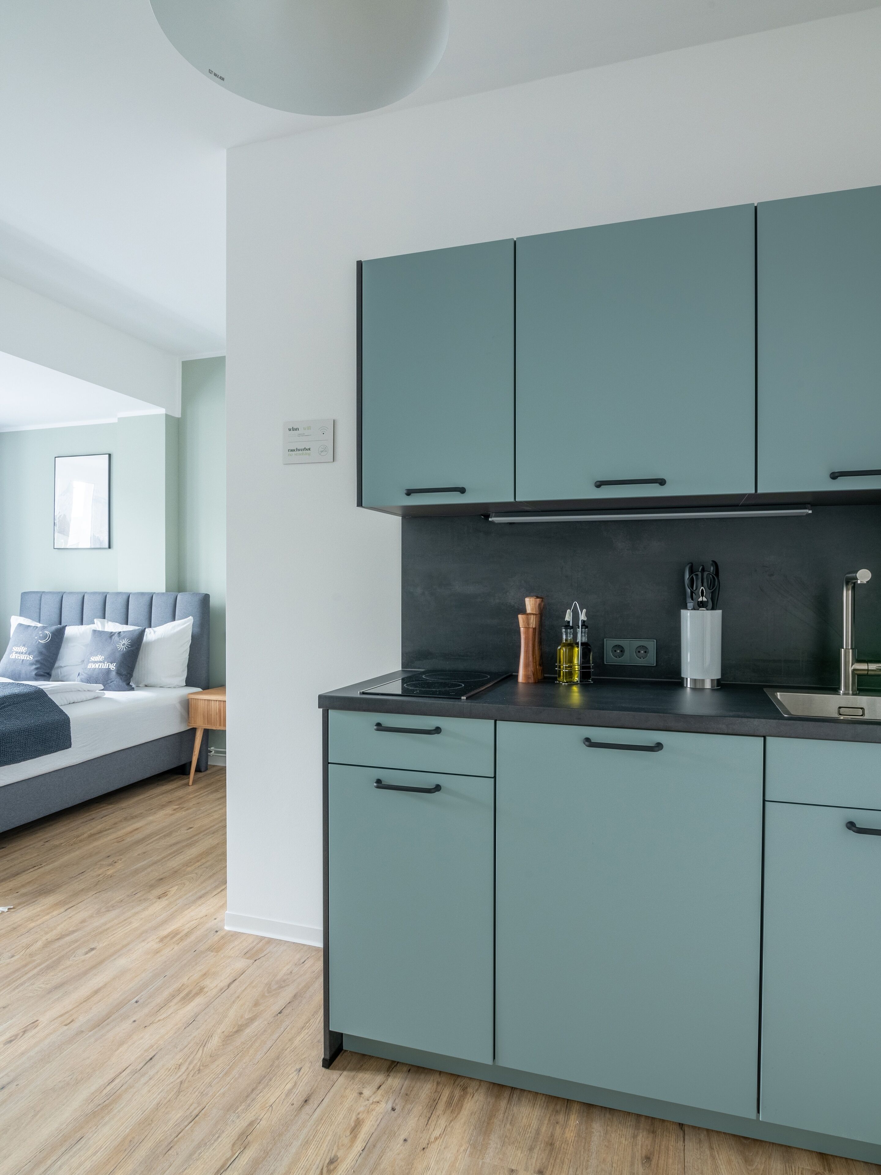 Una cocina moderna con gabinetes color turquesa, encimera negra y estufa integrada.