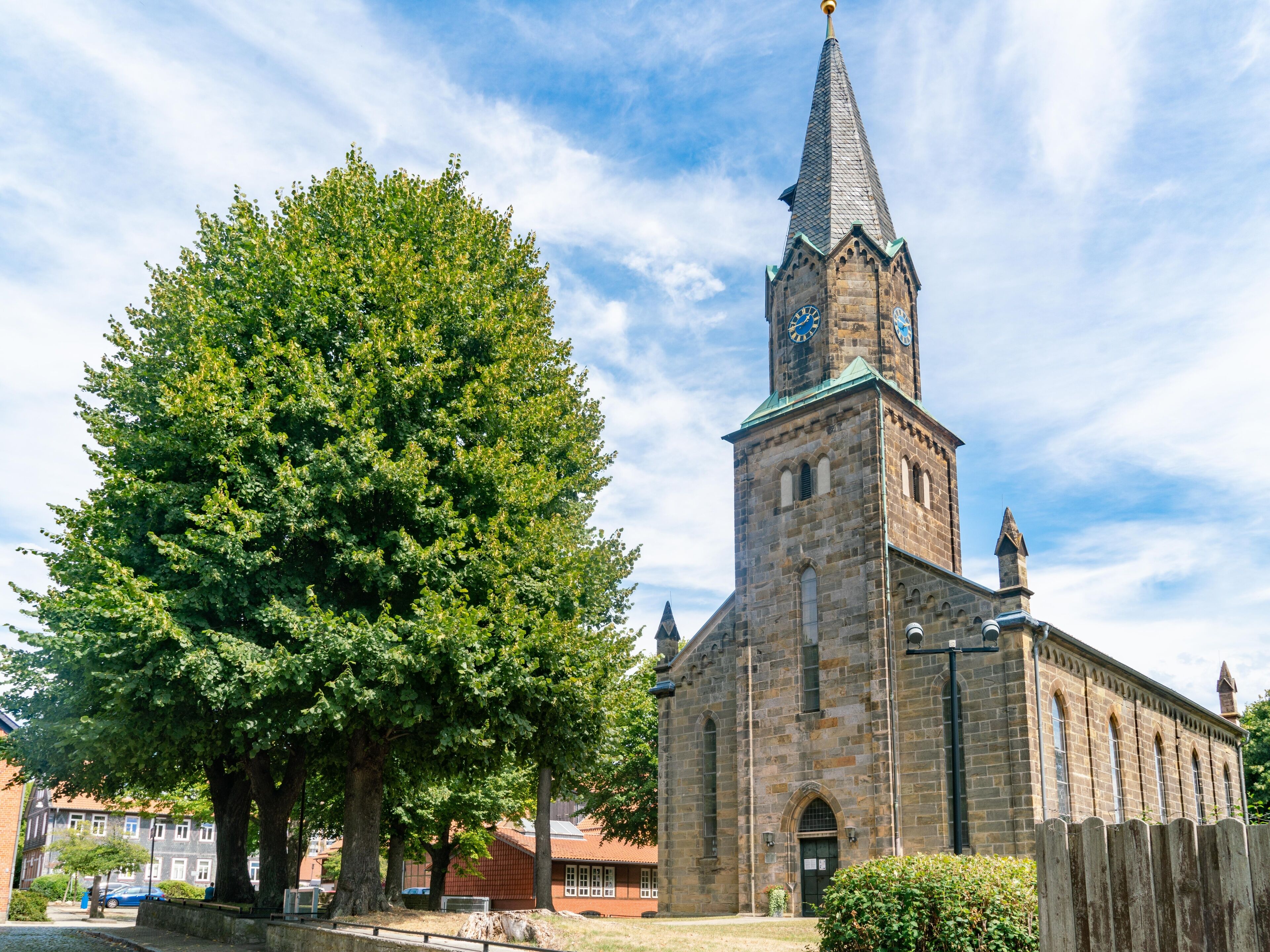 A historic church with a tall steeple and a large tree in front.