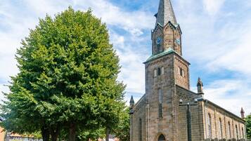 A historic church with a tall steeple and a large tree in front.