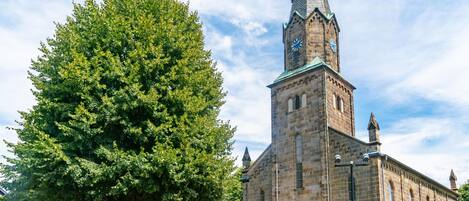 A historic church with a tall steeple and a large tree in front.