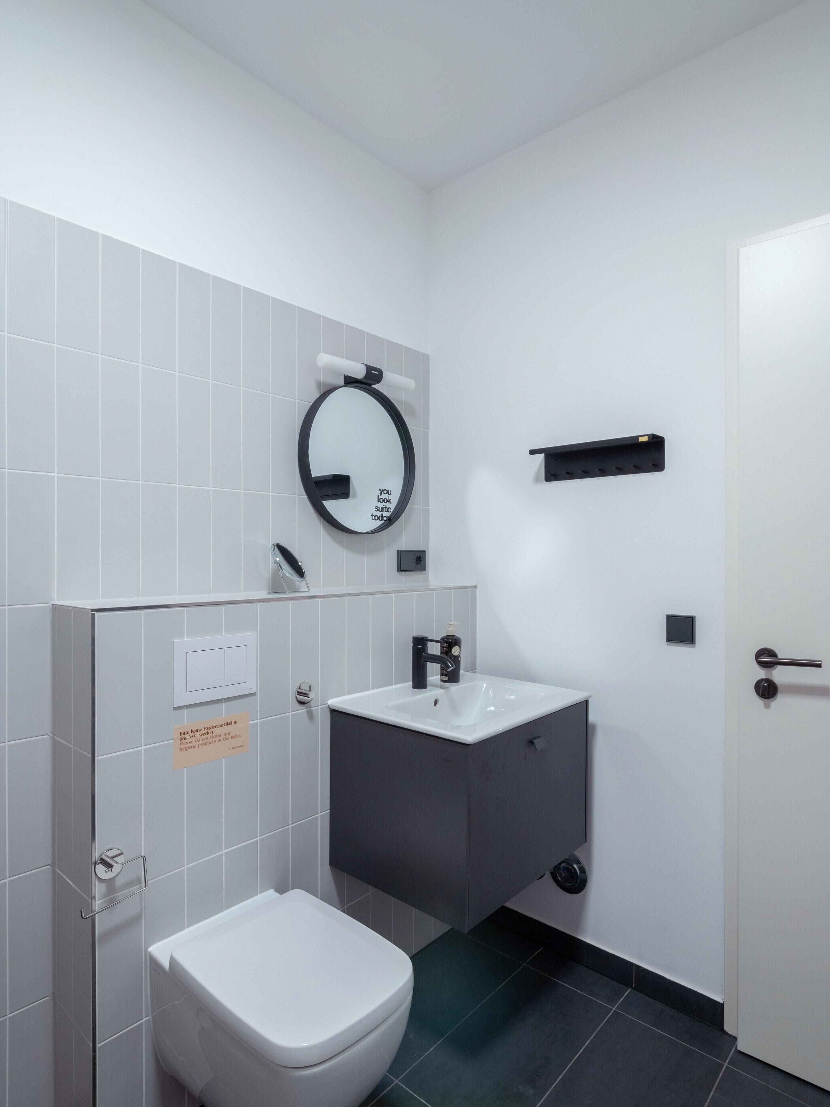 A compact bathroom with a white toilet, a black sink, and a mirror.
