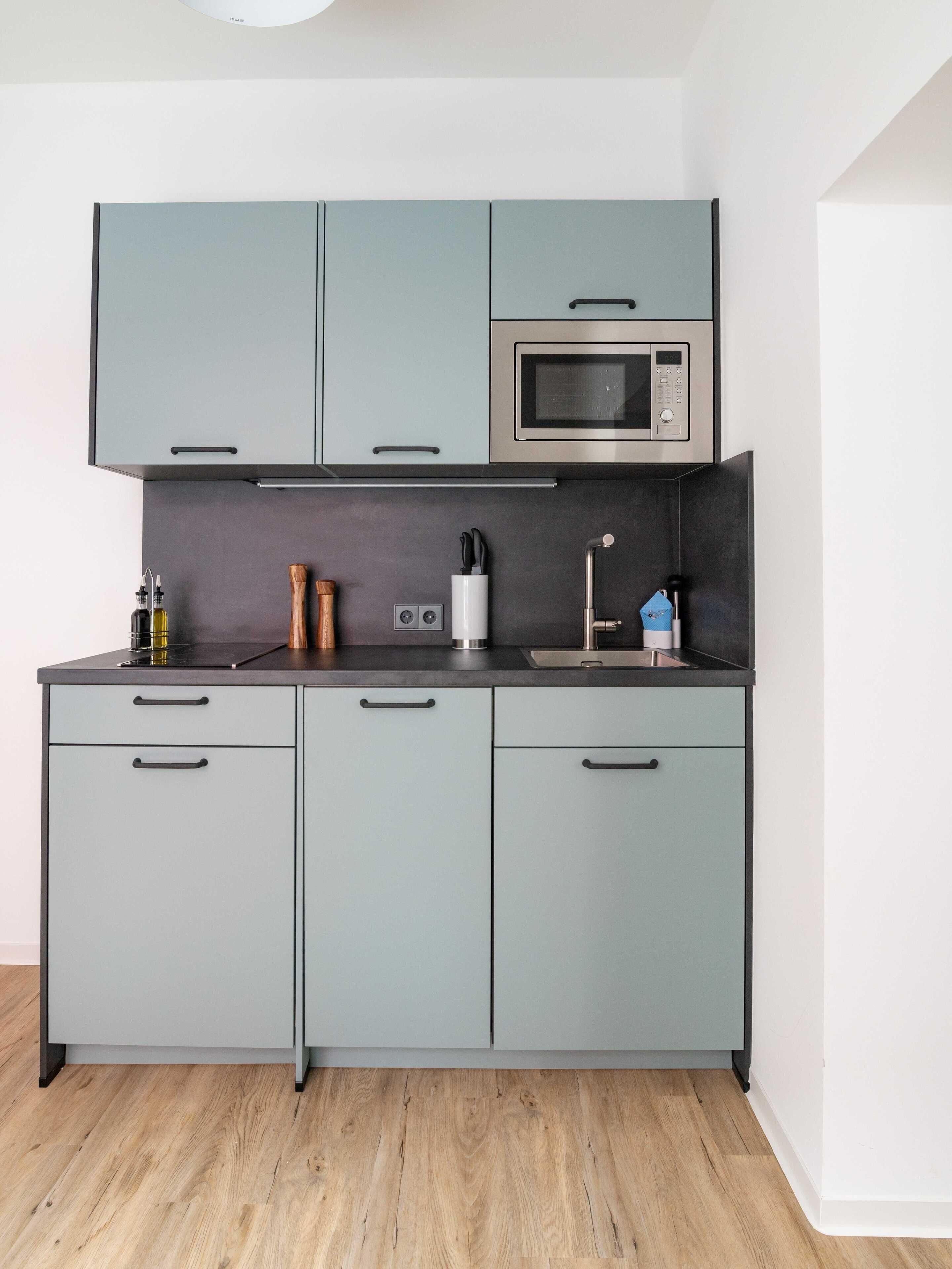 A kitchen with grey cabinets, a microwave, a sink, and a coffee machine.