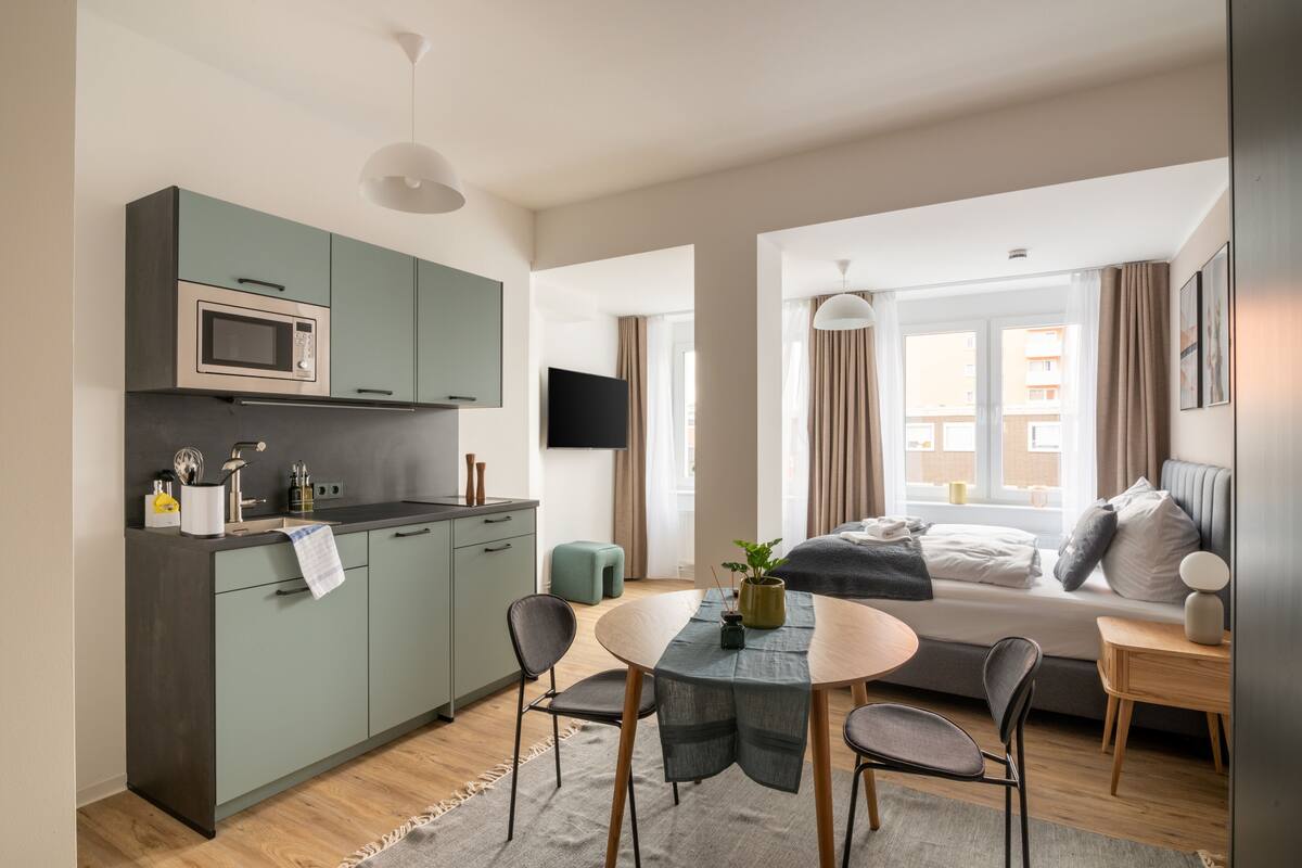 A compact hotel room with a kitchenette, a dining area, a bed with a view, and a TV.
