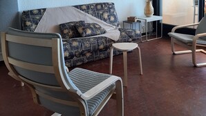 Ein Wohnzimmer mit einer Couch, zwei Sesseln, einem kleinen Tisch und einem großen Fenster.