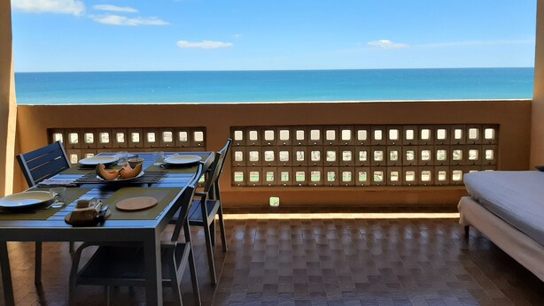 Ein Balkon mit einem Tisch für zwei Personen, mit Blick auf einen Strand.