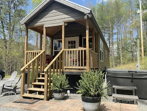 A cabin with a wooden deck, a porch, and a hot tub.