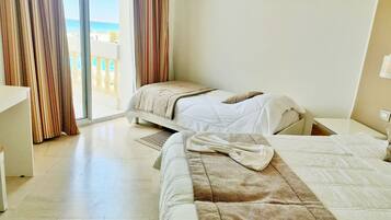 Une chambre d’hôtel avec deux lits, une grande fenêtre avec des rideaux, une vue sur la mer et un sol carrelé.