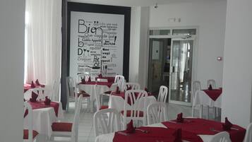 Un comedor con mesas y sillas blancas, servilletas rojas y una pared grande con diversas palabras relacionadas con la comida.
