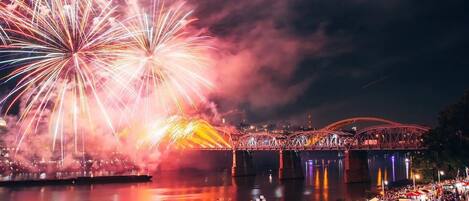 A nighttime outdoor event with fireworks, a crowd, and a bridge.