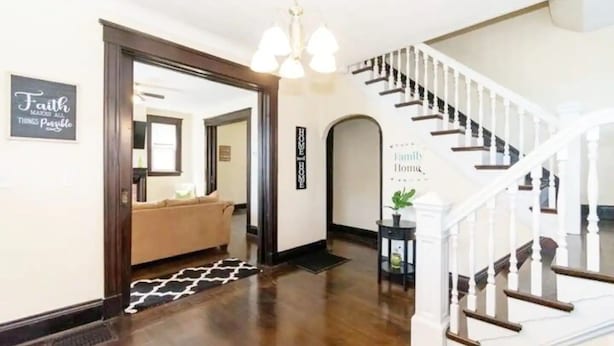 Un pasillo amplio con piso de madera, un sofá color beige y una escalera con barandillas blancas.