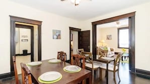 Comedor con mesa de madera dispuesta para cuatro, sillas a cada lado, y una cocina visible a través de un arco.