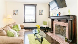 Una sala de estar con un sofá, una mesa de centro de vidrio, una chimenea y un televisor montado en la pared.