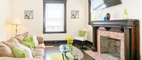 A living room with a sofa, a glass coffee table, a fireplace, and a television mounted on the wall.