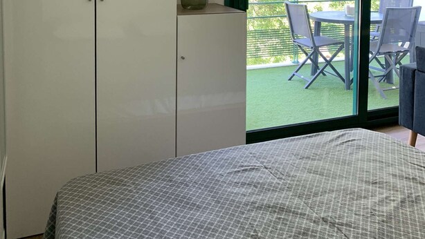 Quarto com cama, guarda-roupa e porta de vidro deslizante que dá para uma área externa com cadeiras e mesa.