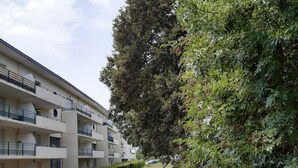 Um edifício residencial com vários andares, varandas, um caminho pavimentado e muita vegetação.