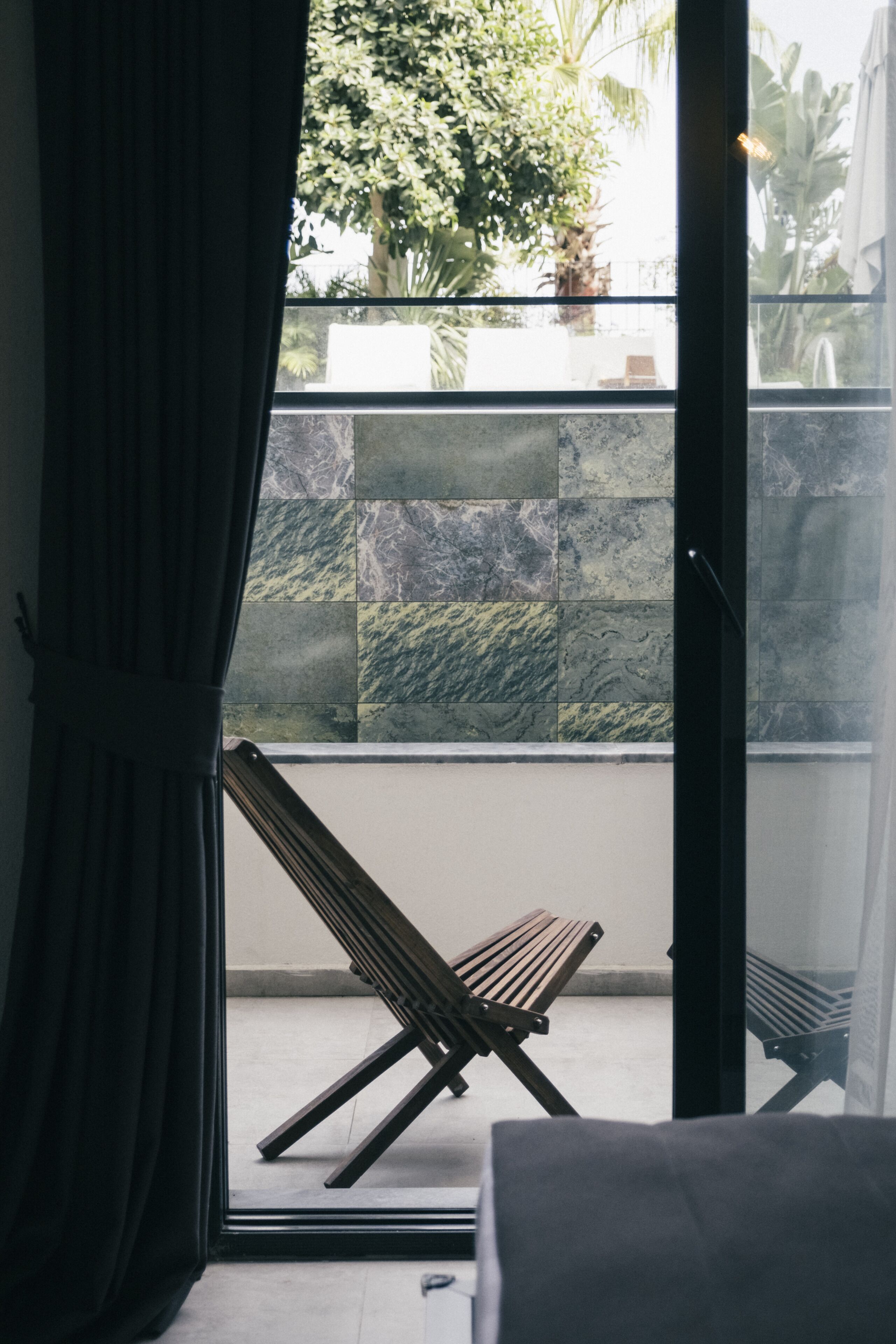 A room with a view of a tiled wall and a wooden bench outside.