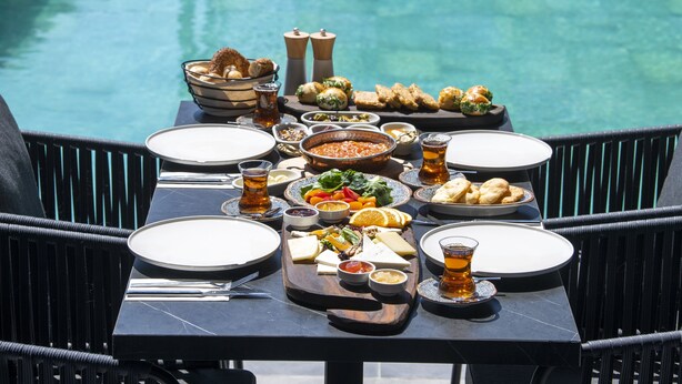 Une table à manger dressée avec différents plats et boissons, donnant sur une piscine.