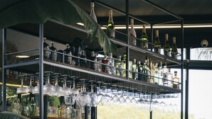 Un espace bar doté de plusieurs étagères remplies de bouteilles et de verres, de tabourets de bar en bois et offrant une vue sur la verdure à l’extérieur.