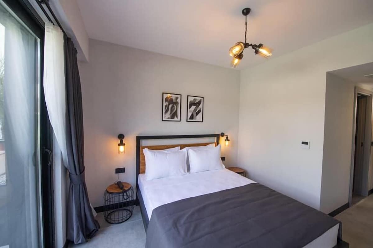 A bedroom with a bed, two wall-mounted light fixtures, a ceiling light, and two framed pictures on the wall.