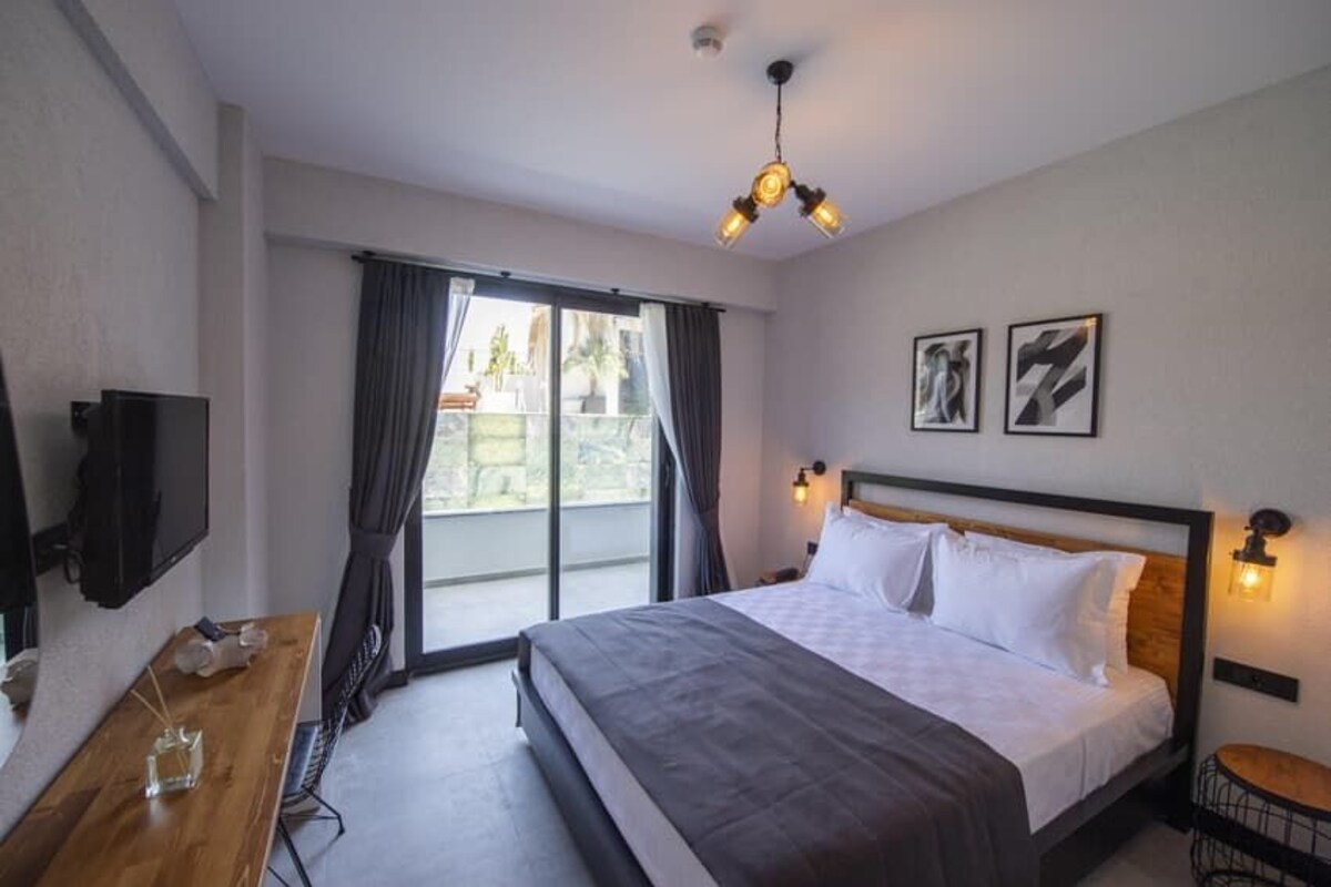 Una habitación de hotel con una cama, un televisor, una mesa de madera y un balcón con cortinas.