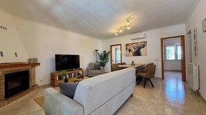 Ett vardagsrum med en öppen spis, en tv, en soffa, ett matbord med stolar och konstverk på väggarna.