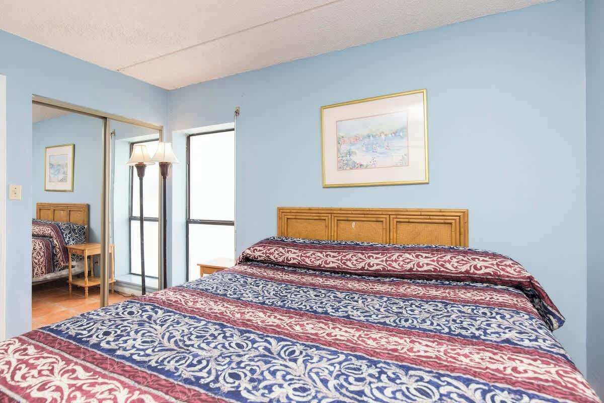 Une chambre à coucher avec un lit, une tête de lit en bois, un tableau encadré au mur et une lampe sur pied.