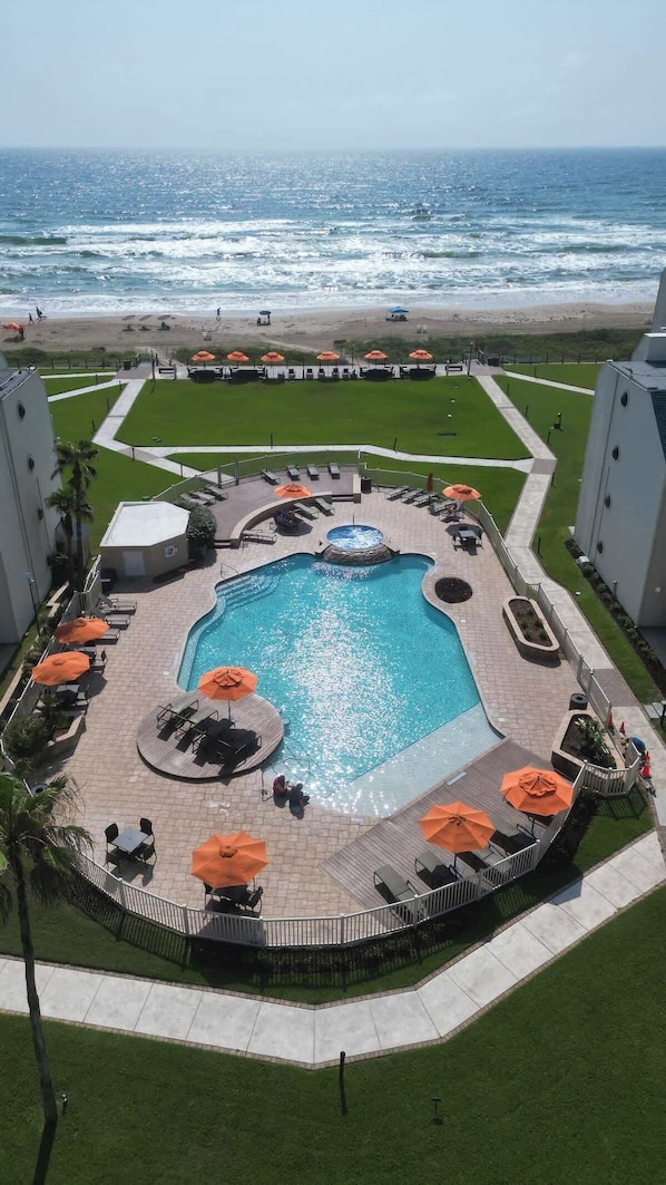 A pool area with a view of the ocean, surrounded by lounge chairs and umbrellas.