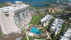 Un hotel con varios pisos, piscina y vistas del entorno, incluyendo un cuerpo de agua y otros edificios.