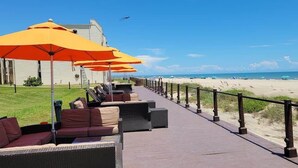 Un paseo marítimo frente a la playa con asientos exteriores y sombrillas, con vista a la playa y al océano.