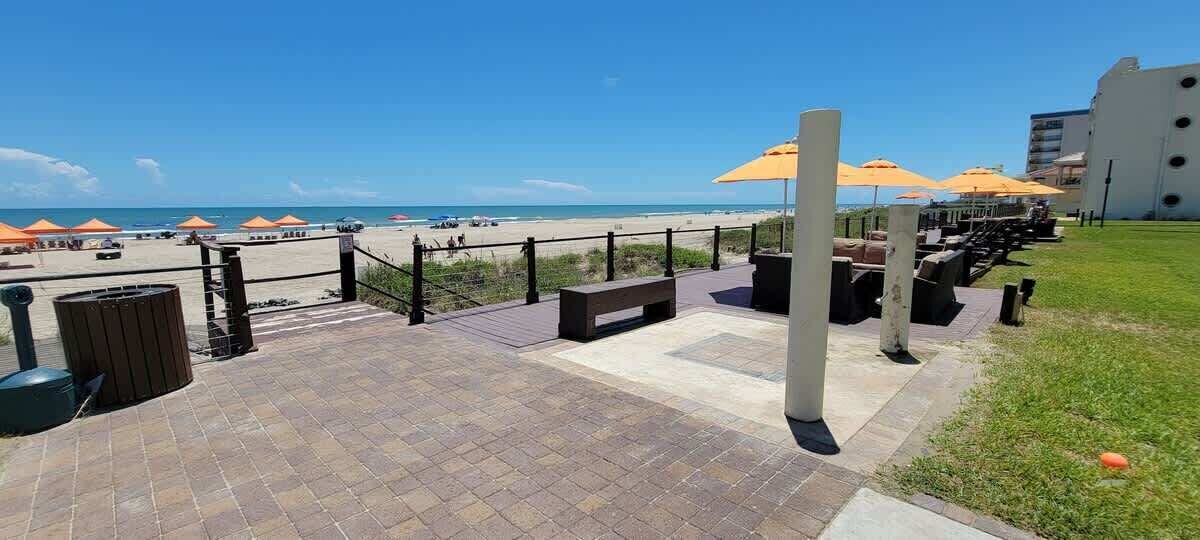 Un patio frente a la playa con mesas y sillas al aire libre y sombrillas, con vista al mar.
