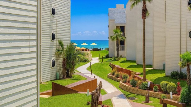 Un resort con un camino que lleva a una zona de piscina, rodeado de palmeras y vista al océano.