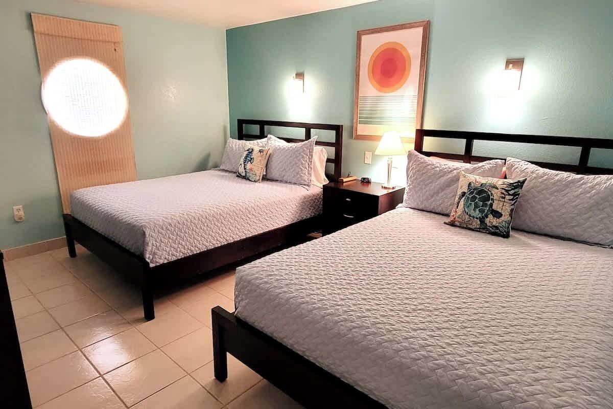 Dos camas individuales con cabeceros, una mesita de noche, una lámpara de pared y un cuadro en la pared.