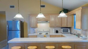 A kitchen with wooden cabinets, a stainless steel refrigerator, a white stove, and three wooden stools.
